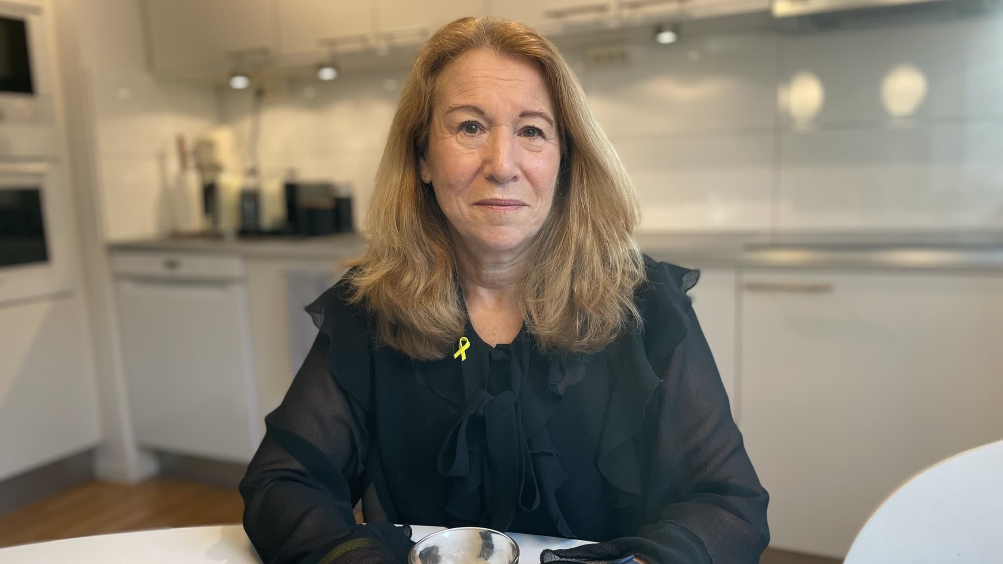 En kvinna sitter vid ett köksbord med en kaffe i handen