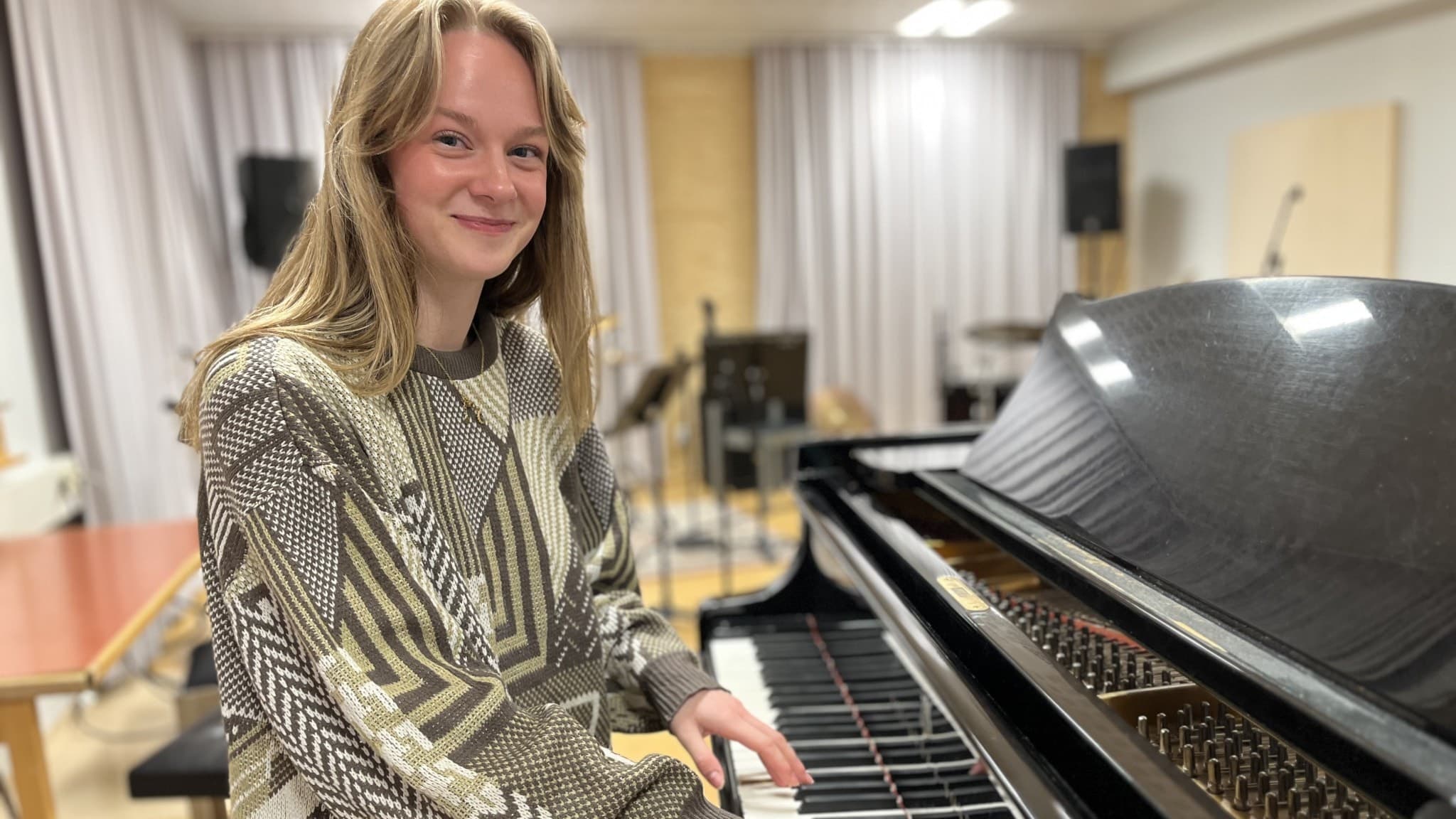 Ida Andersson spelar på ett svart piano i ett musikrum med högtalare och mikrofoner i bakgrunden.