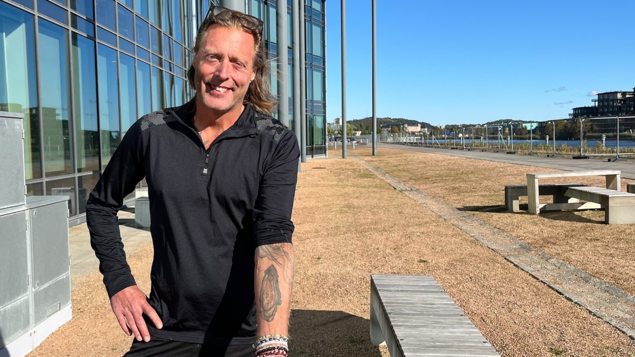 Kocken Gustav Trägårdh står utomhus vid en modern byggnad med glasfasad. Han bär en svart tröja och ler mot kameran. 