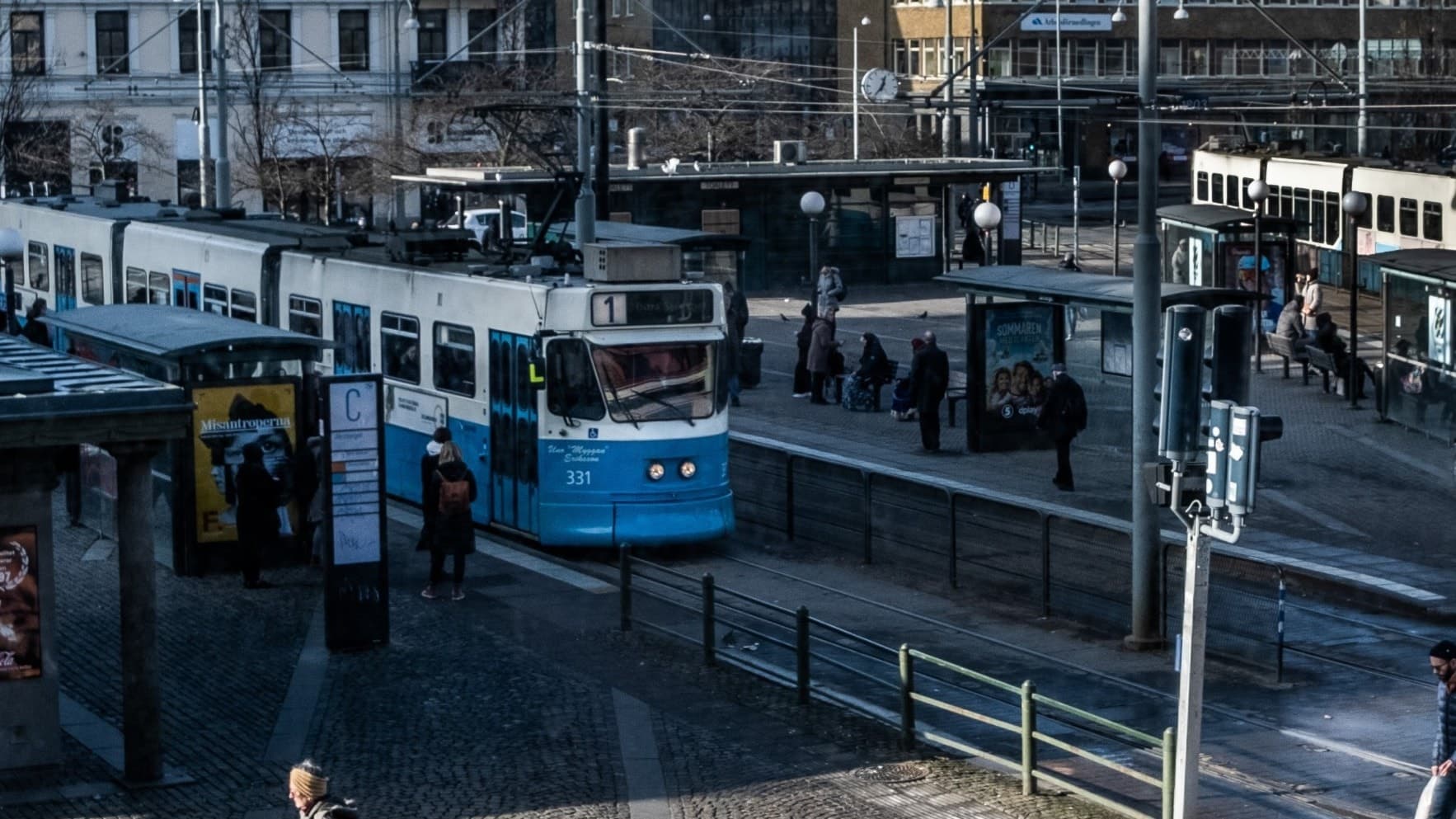 Spårvagn vid Järntorget i Göteborg med människor som väntar vid hållplatsen. Trafikljus och skyltar syns, där högersvängen är avstängd för omledning av trafiken.