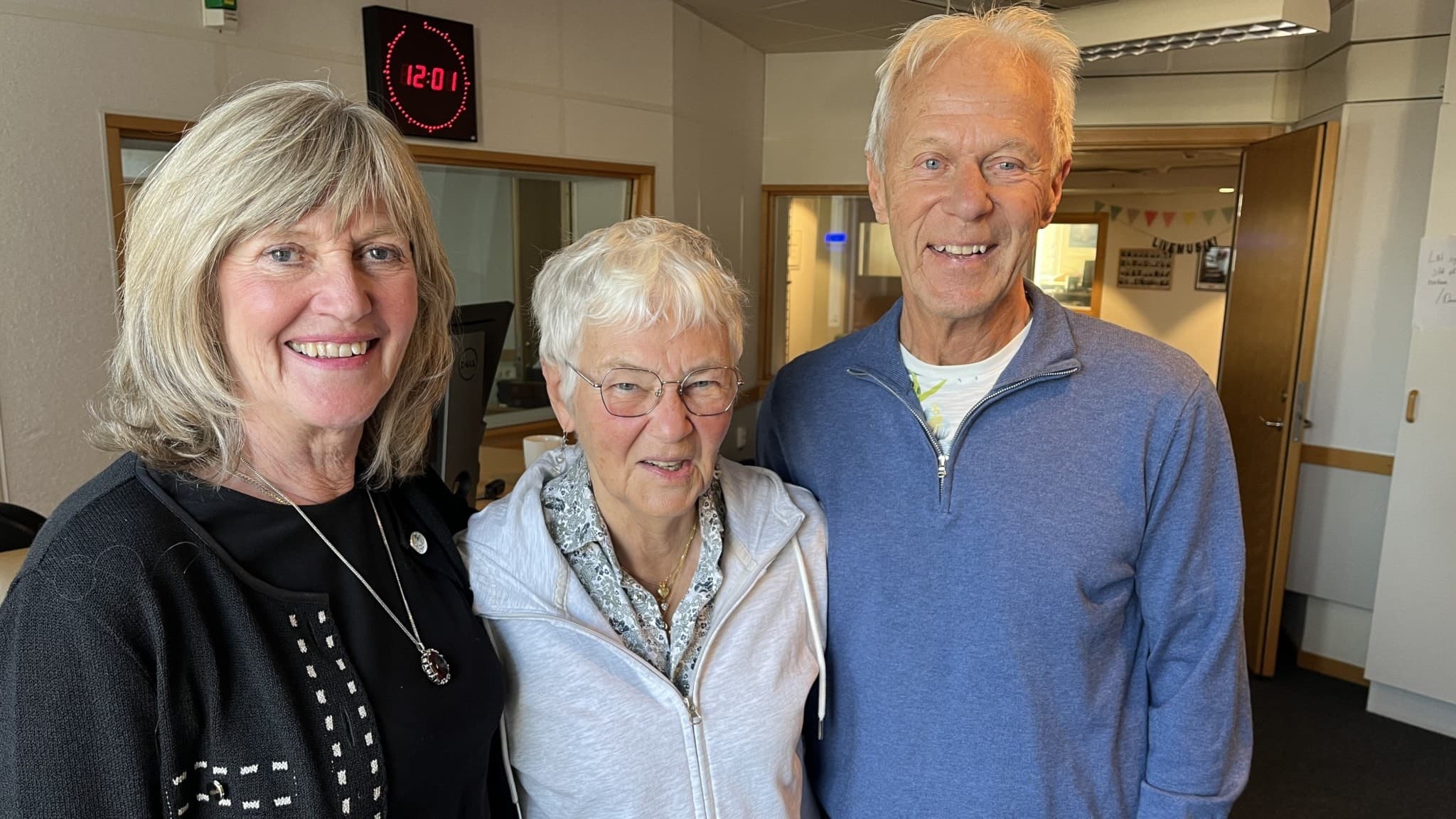 Anki Nilsson, Madeleine Svensson och Rolf Thanche står tillsammans i en radiostudio med fokus på en ljus inomhusmiljö och en digital klocka på väggen i bakgrunden.