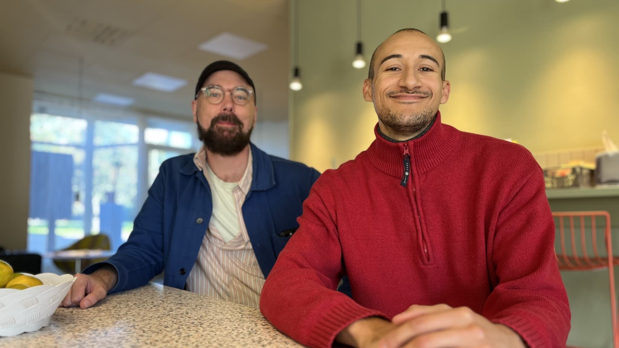 Martin Forsberg och Ruben Brown från Norrdans sitter vid ett bord i en ljus lokal med modern inredning. En skål med citroner står på bordet och lampor hänger från taket i bakgrunden.