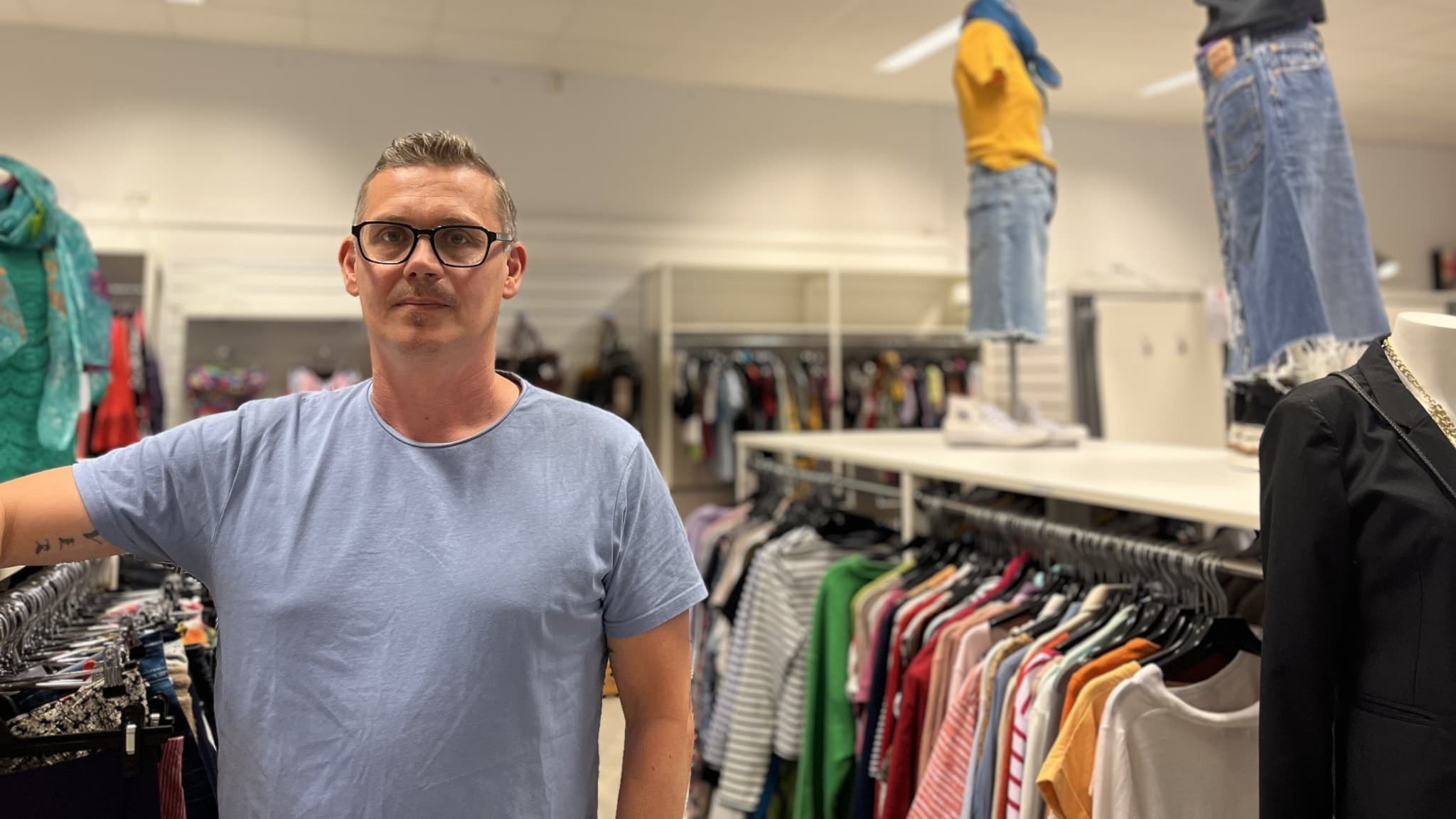 Andreas Lundgren står i en secondhandbutik bland klädställningar fyllda med färgglada plagg. Hyllor med jeans och andra klädesplagg syns i bakgrunden.