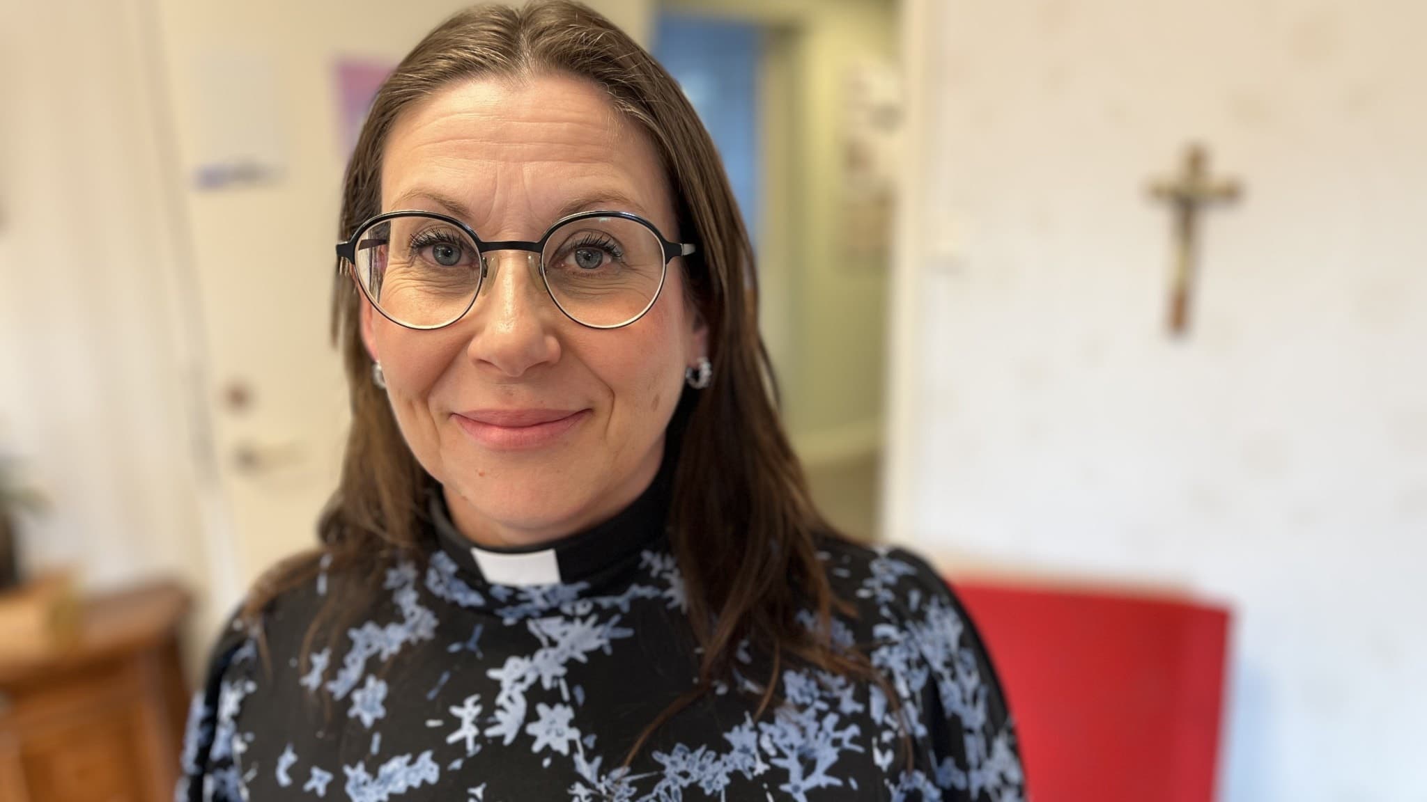 Petra Hamnström, församlingsherde Tuna-Attmars och Stöde församlingar. Hon står inomhus och i bakgrunden syns en vit vägg. Hon har utsläppt hår och glasögon.