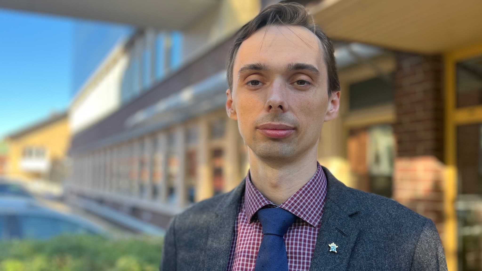 En man poserar för ett porträtt utanför Tingsrätten i Sundsvall. Han är klädd i mörk kavaj, rutig skjorta och blå slips.