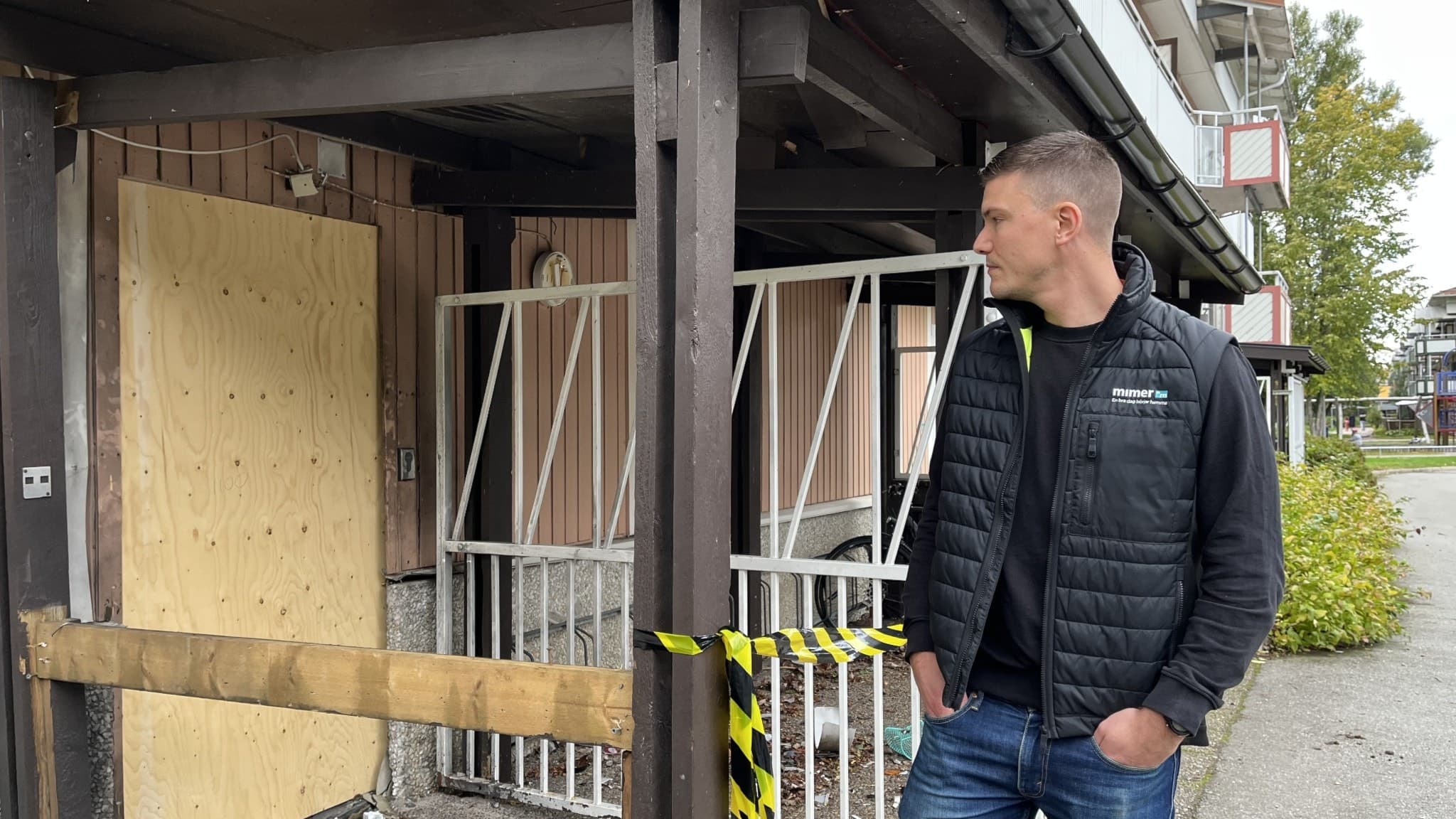 Martin Björnberg, distriktschef på Mimer, står framför en skadad byggnad med avspärrningsband och en igenspikad dörr. Han är klädd i en svart jacka och jeans.