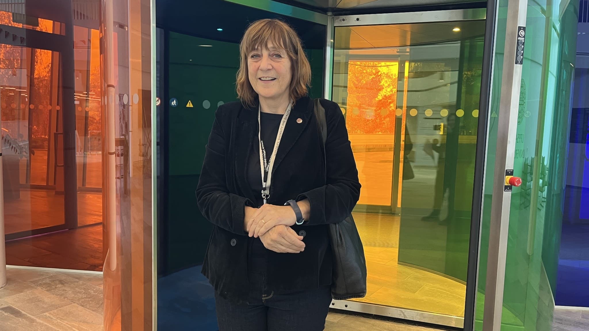 Pernilla Björk, kommunikationsdirektör vid Uppsala universitet, står framför en glasdörr med färgglada reflektioner. Hon bär en mörk kavaj.
