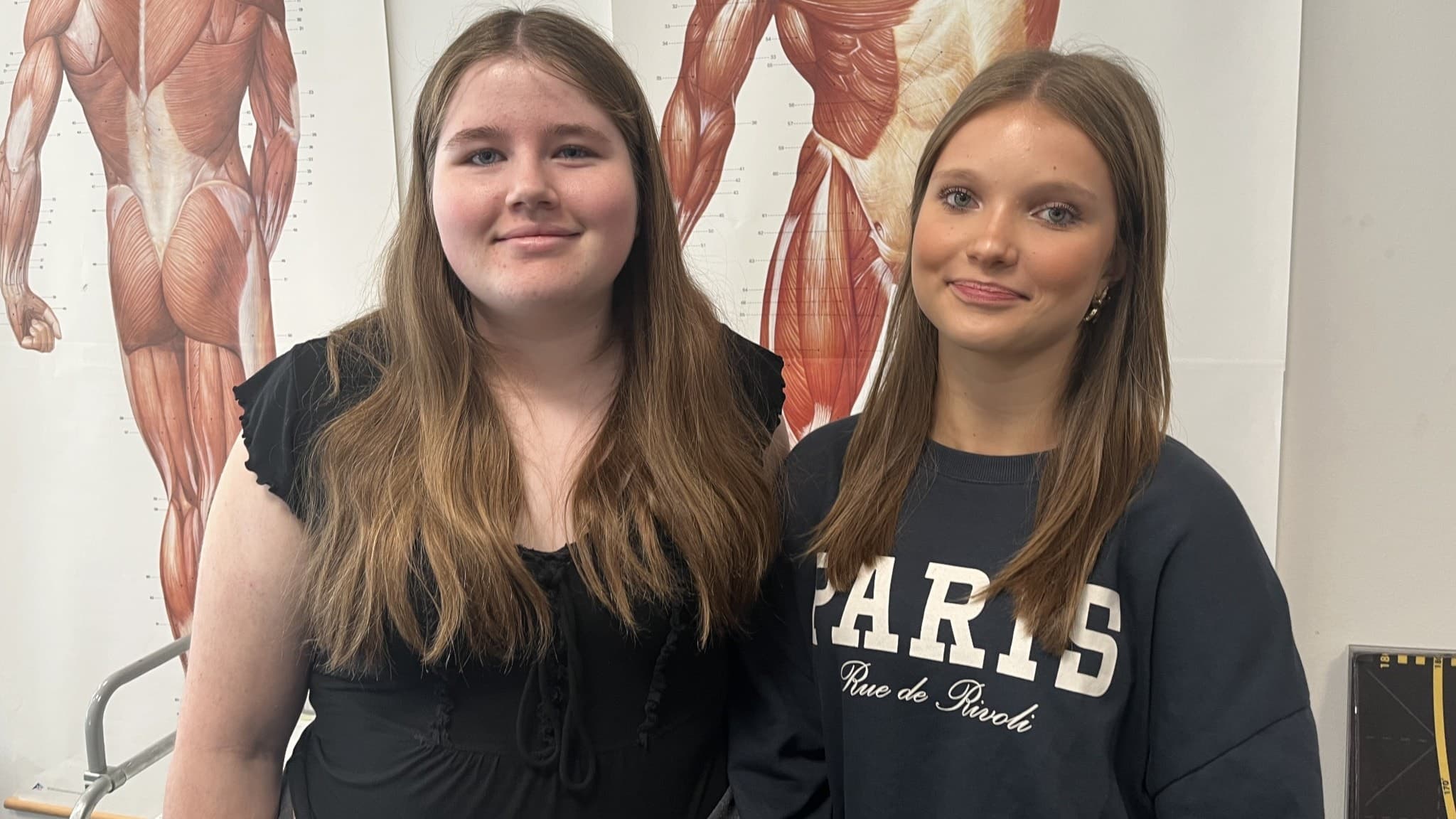 Meja Kettunen och Maja Adolfsson står i ett rum på Halmstad högskola med anatomiska affischer i bakgrunden. De deltar i en rundtur på högskolan.