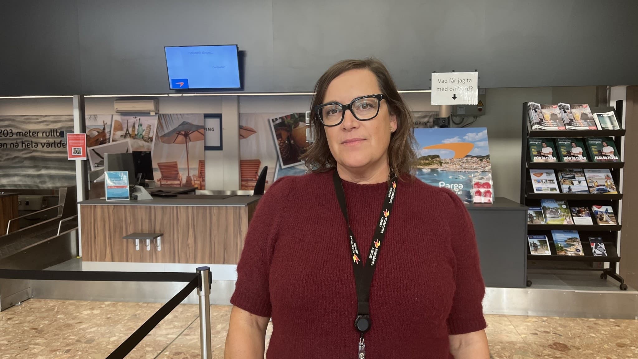Jessica Ågren Ohlson, marknadschef på Norrköping Airport, står inomhus vid incheckningsdisken på flygplatsen, omgiven av broschyrställ och en skärm i bakgrunden.