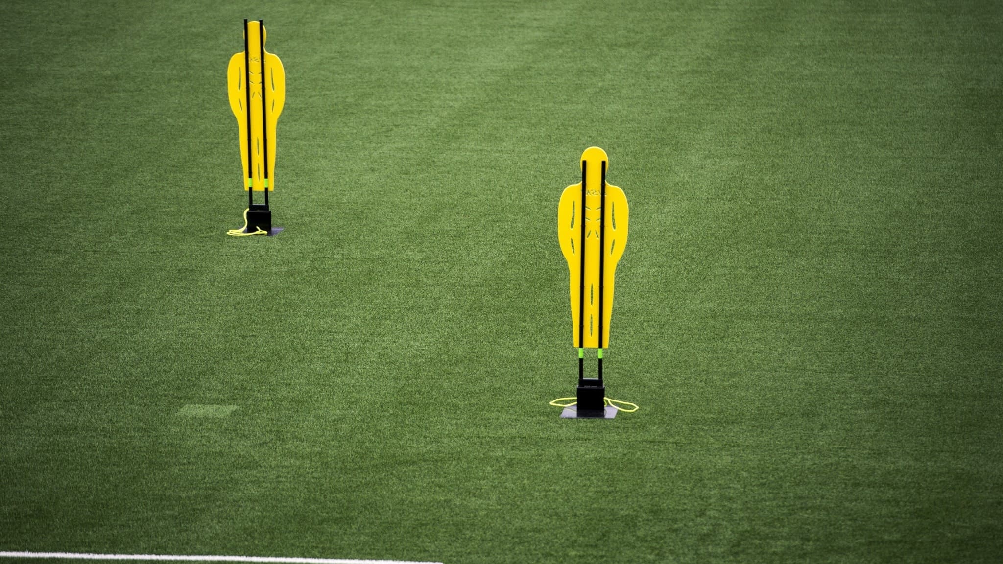Två gula träningsfigurer står på en fotbollsplan med grön konstgräs vid Viking stadion i Stavanger, Norge. Bilden visar förberedelser för fotbollsträning.