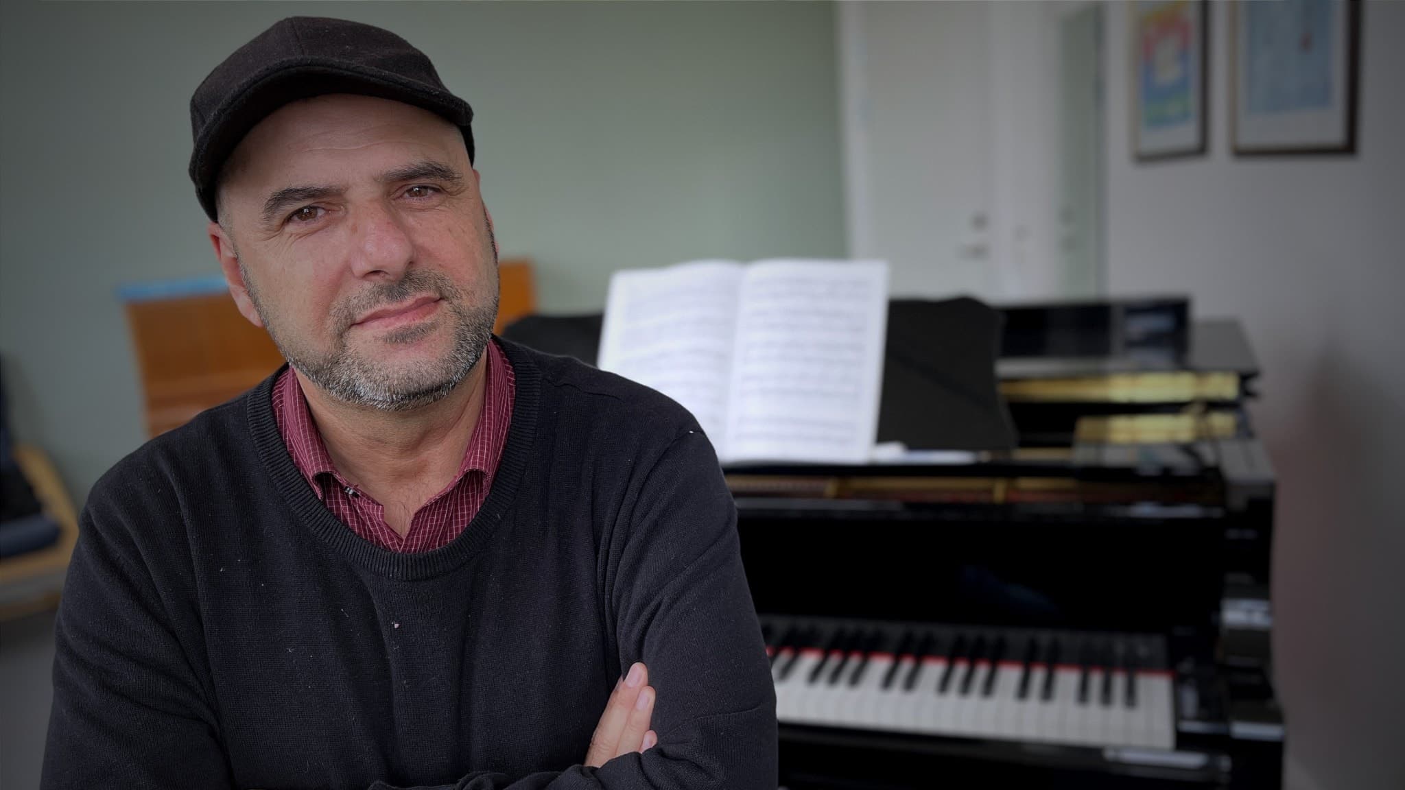 Faiez Michail, musikskolan i Orsas ende pianolärare, står framför ett svart piano med uppslagen notbok i ett klassrum.
