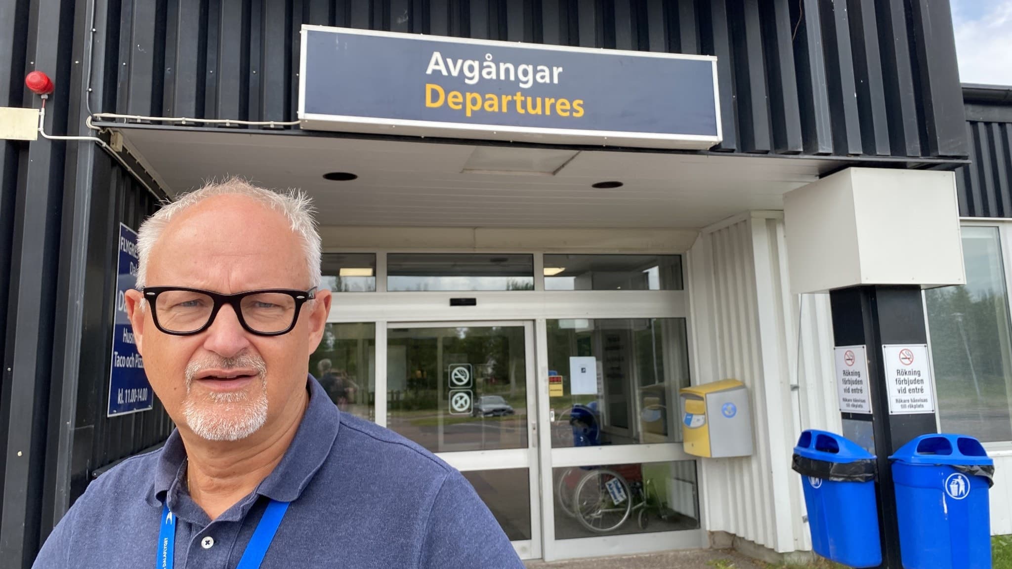 Stefan Carlsson står  framför en entré till flygplatsen Dala Airport. Han har glasögon och grått skägg.