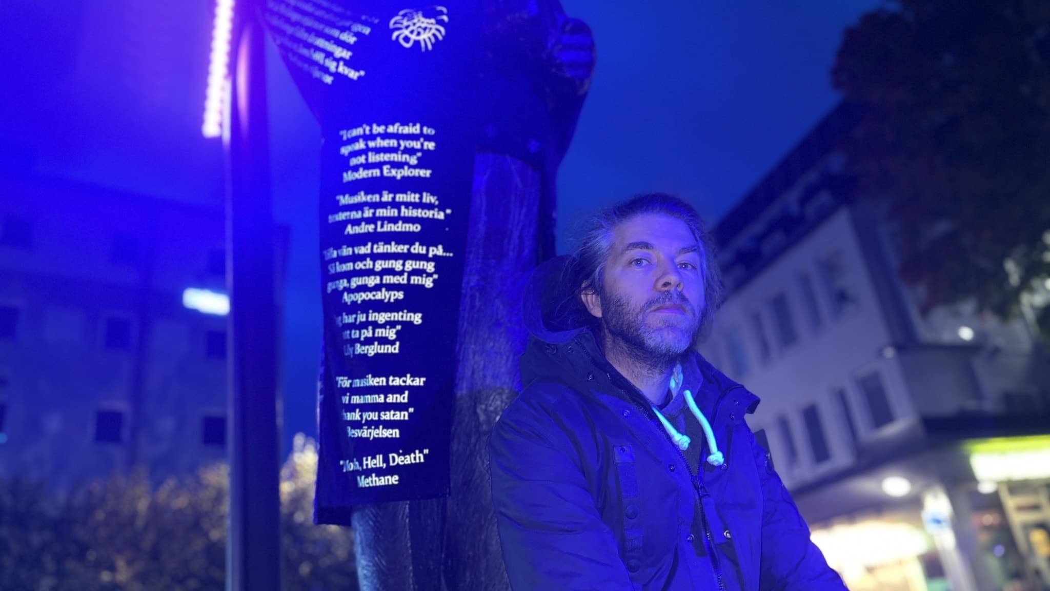 Zacharias Vindbacke, kostymör, står bredvid Jussi Björling-statyn, som är klädd i en svart dräkt med text. Statyn är belyst i blått, och stadsmiljö syns i bakgrunden.