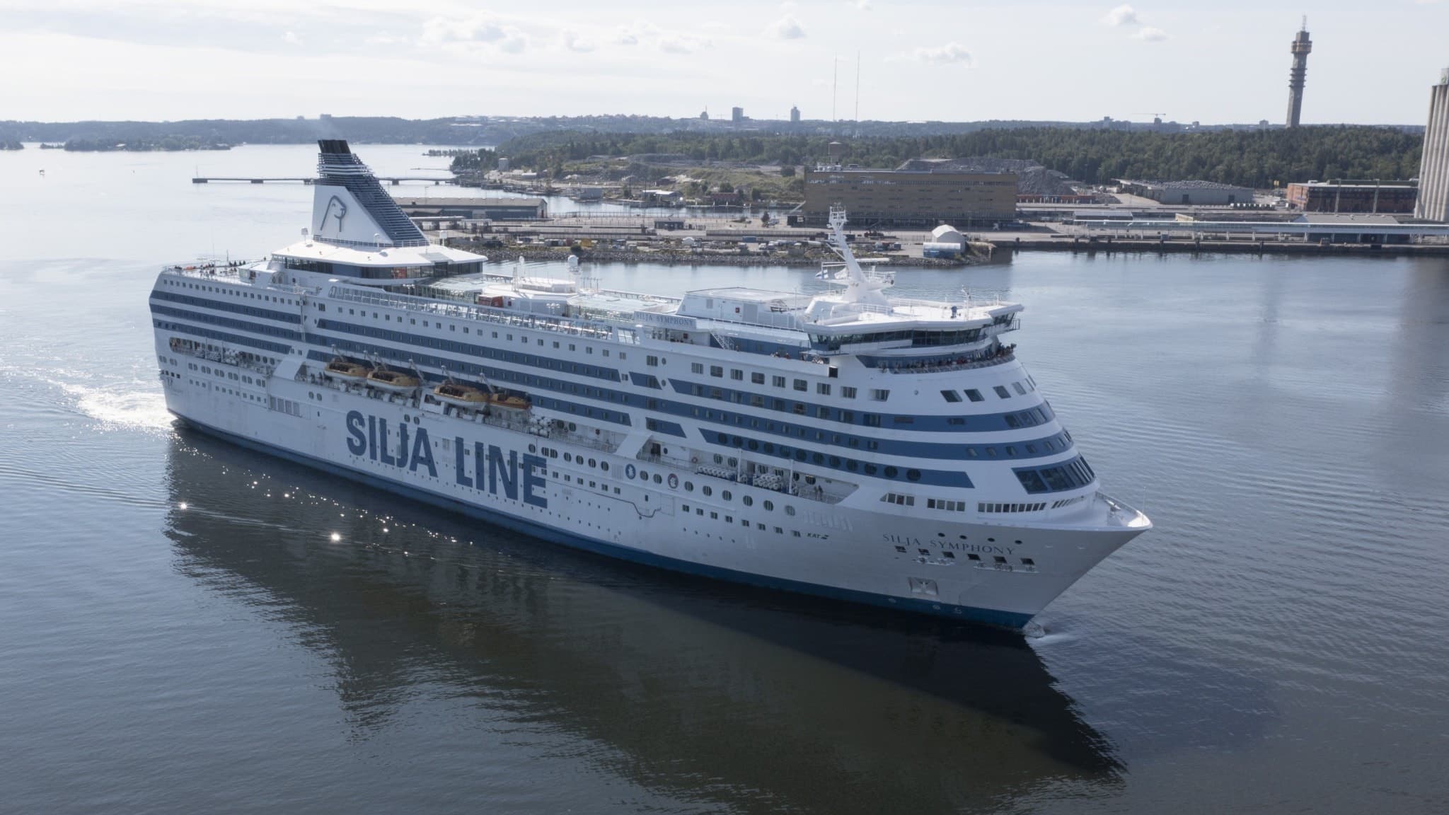 En Finlandsfärja anländer till en hamn. Färjan glider fram på stilla vatten med stadens skyline i bakgrunden.