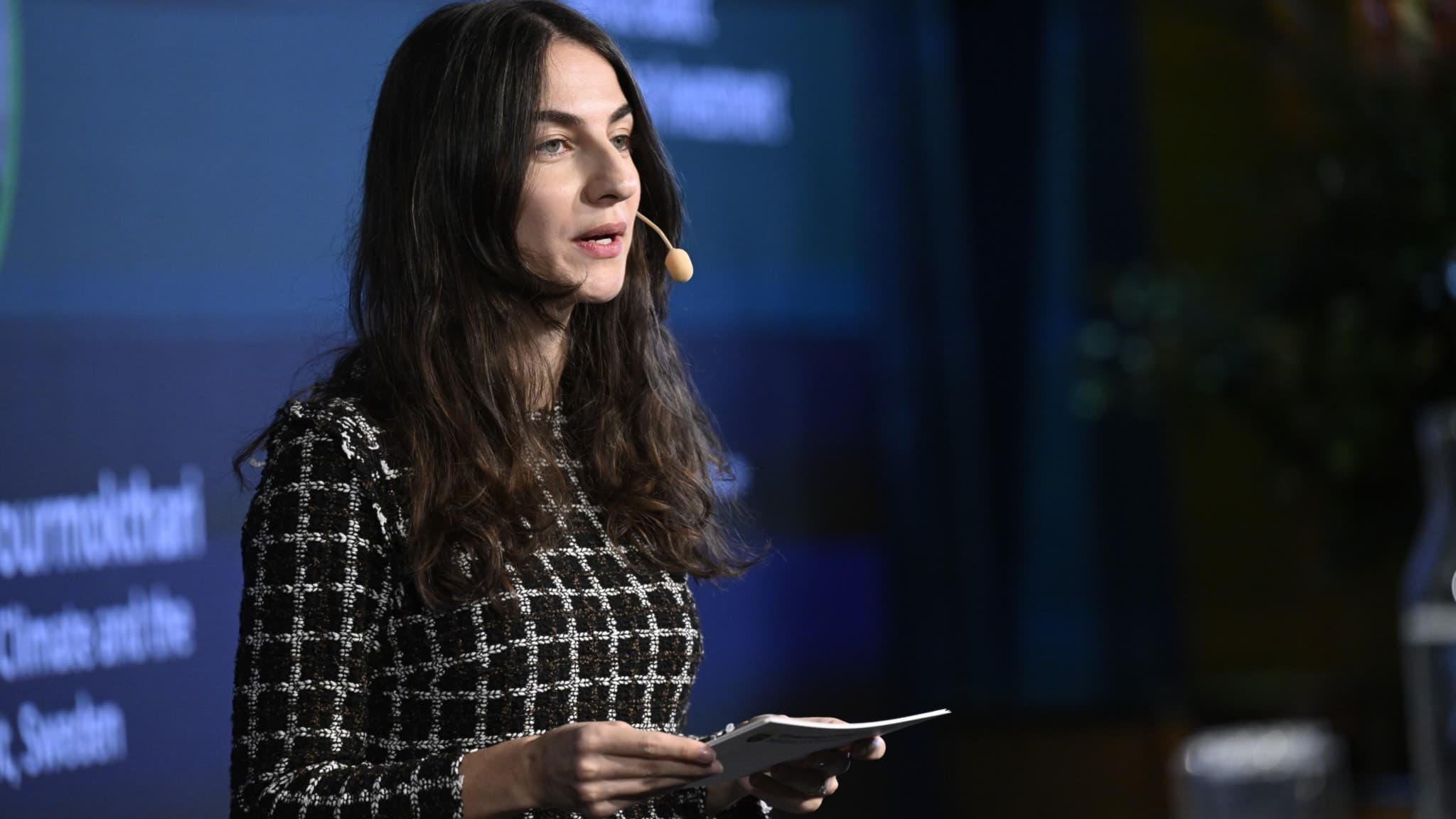 Romina Pourmokhtari, klimat- och miljöminister, talar på Nordic-Baltic Nuclear Investment Summit i Stockholm. Hon håller ett papper och har en mikrofon, med en skärm i bakgrunden.