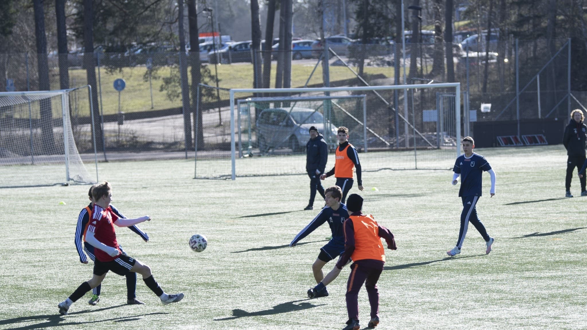 Ungdomar spelar fotboll och det är lätt frost på planen, några av ungdomarna har orangea västar och mössor på sig.
