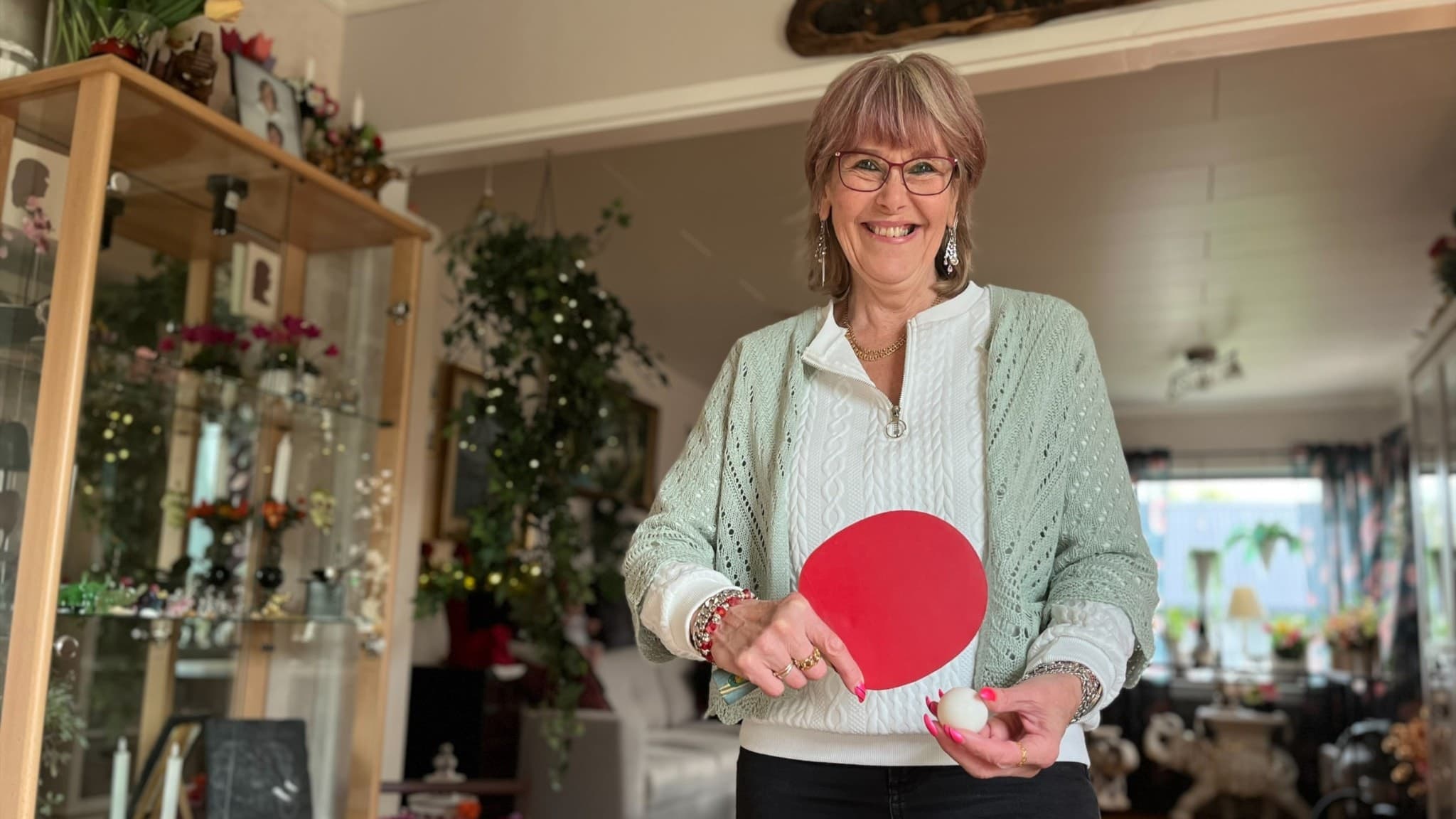 Pirjo Leivo från Karlskoga står inomhus med ett bordtennisracket i handen. Bakgrunden visar ett vardagsrum med växter och heminredning.