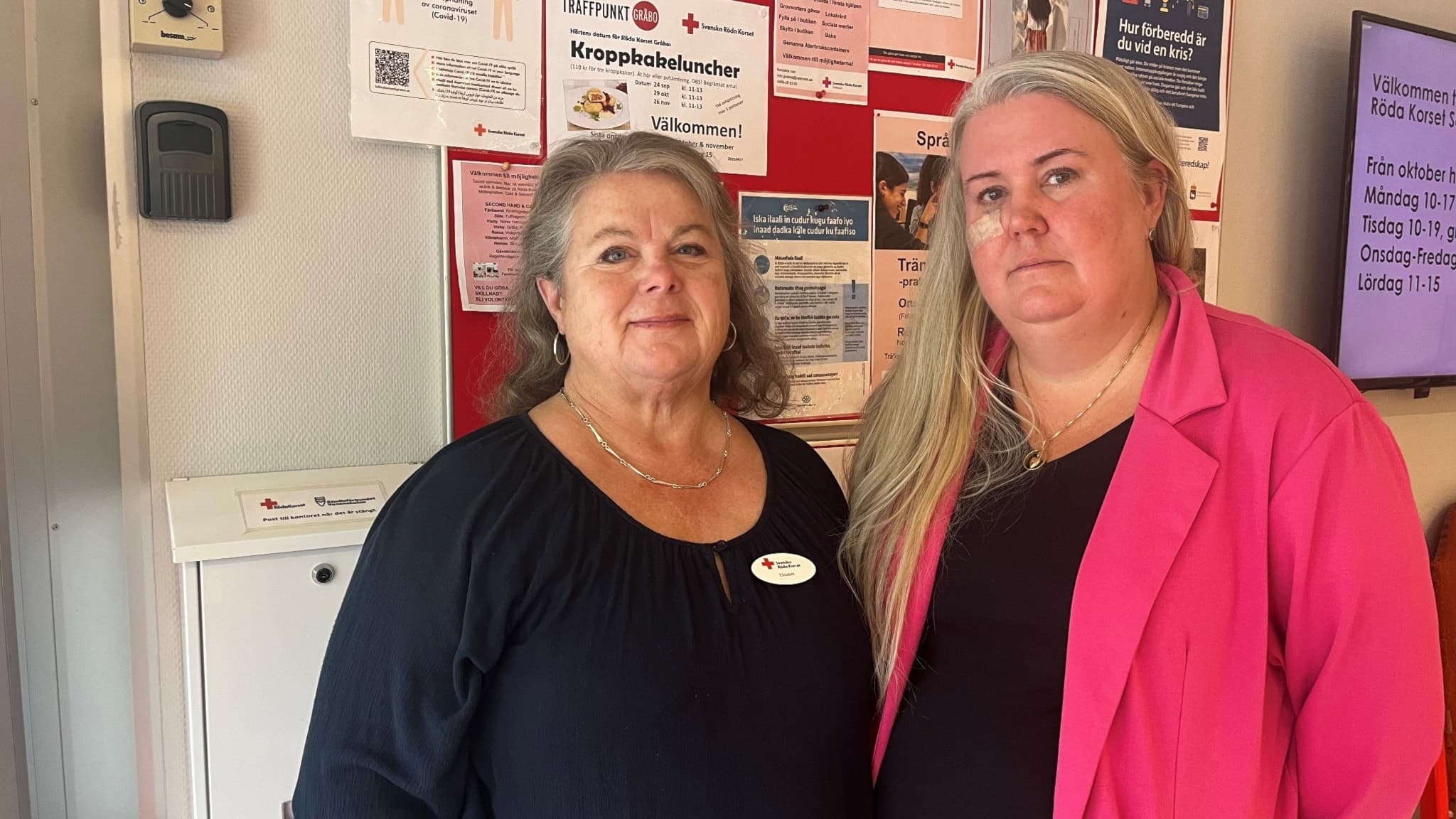 Elisabet Lind och Anna Klintbom från Röda Korset står framför en anslagstavla fylld med informationsblad på Röda Korsets lokaler i Visby.