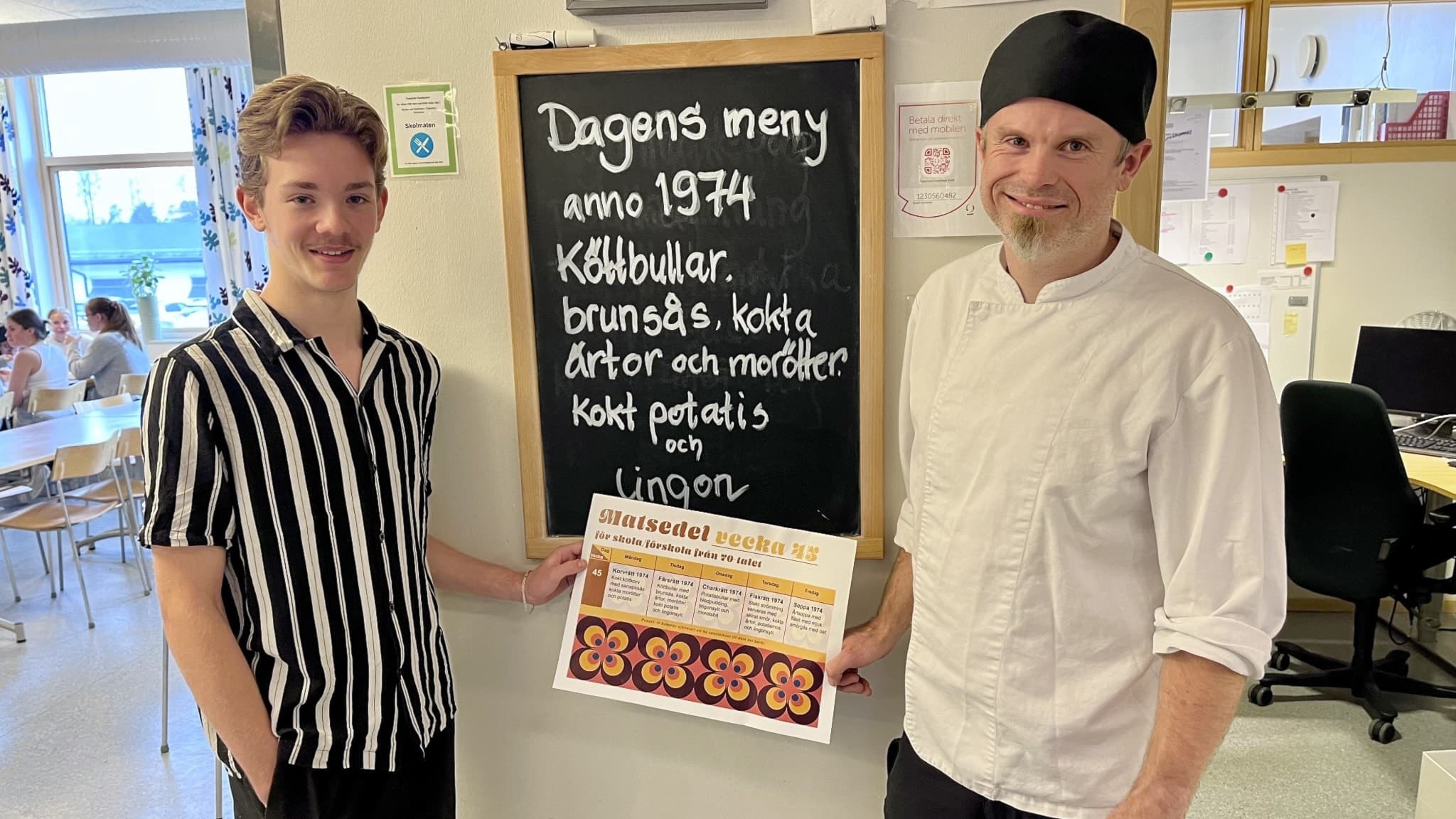 en elev och en skolkökskock håller en matsedel mellan varandra och mellan dem står det "Dagens meny anno 1974" skrivet på en svart tavla. 
