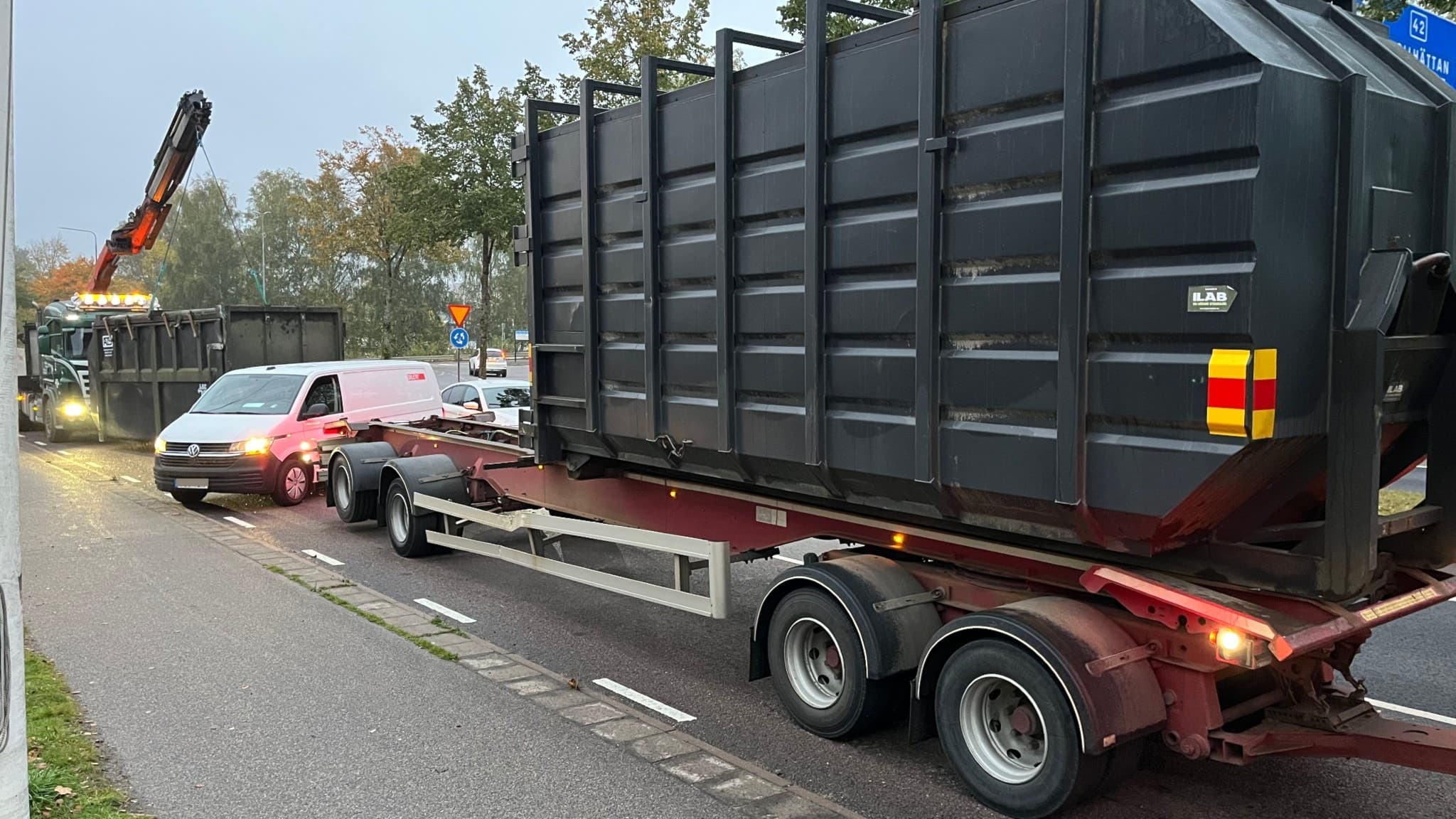 En container på en trailer, ännu en container står på marken, en kranbil syns i bakgrunden.