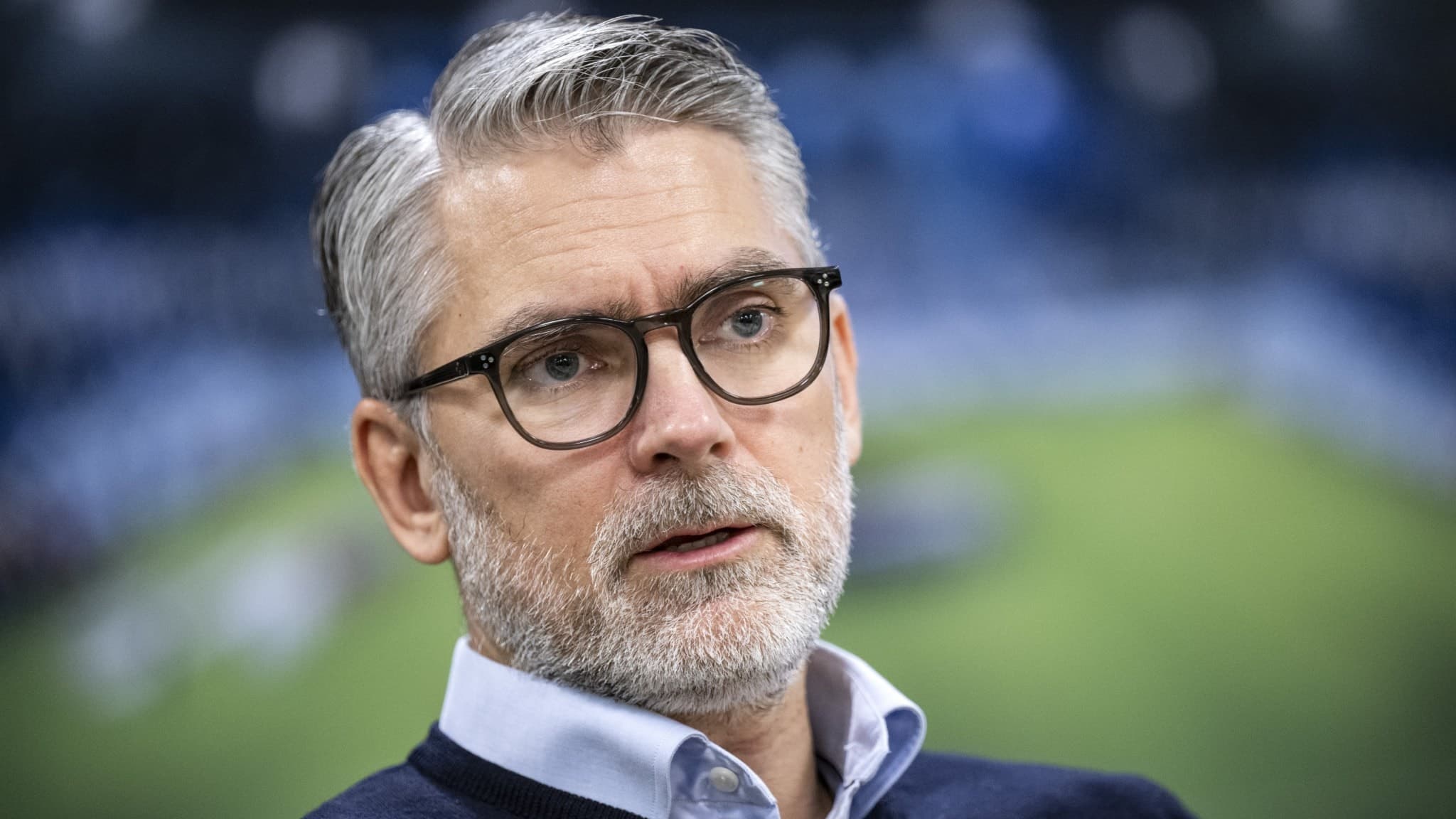 Niclas Carlnén, avgående vd för Malmö FF, klädd i mörk tröja och skjorta, står framför en fotbollsplan på Eleda Stadion i Malmö med suddiga läktare i bakgrunden.