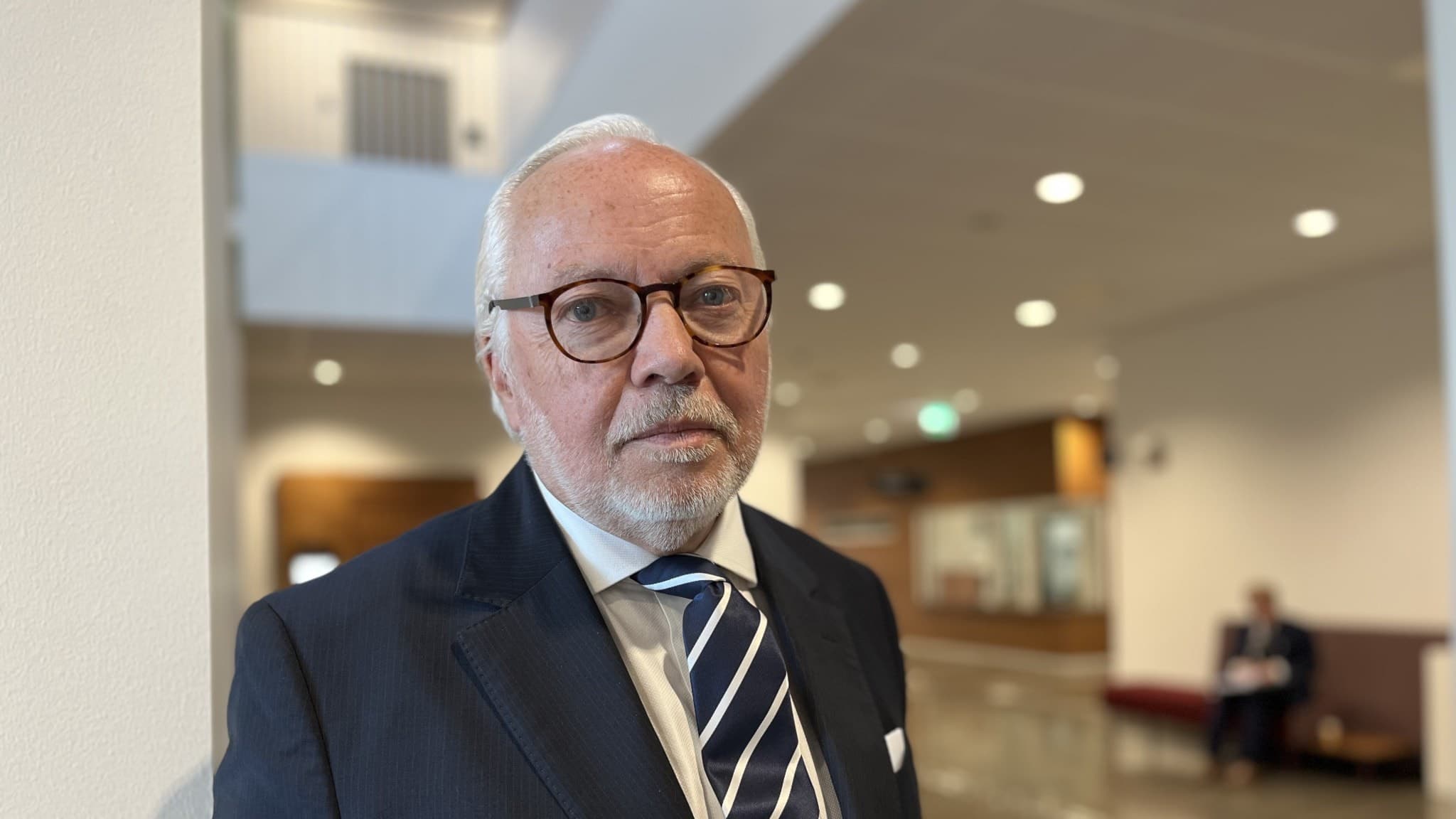 Lars Kruse, advokat, iklädd mörk kostym och randig slips, står i modern rättssalsmiljö vid Helsingborgs tingsrätt. Bakgrunden visar ljusa väggar och personer i samtal vid bänkar. 