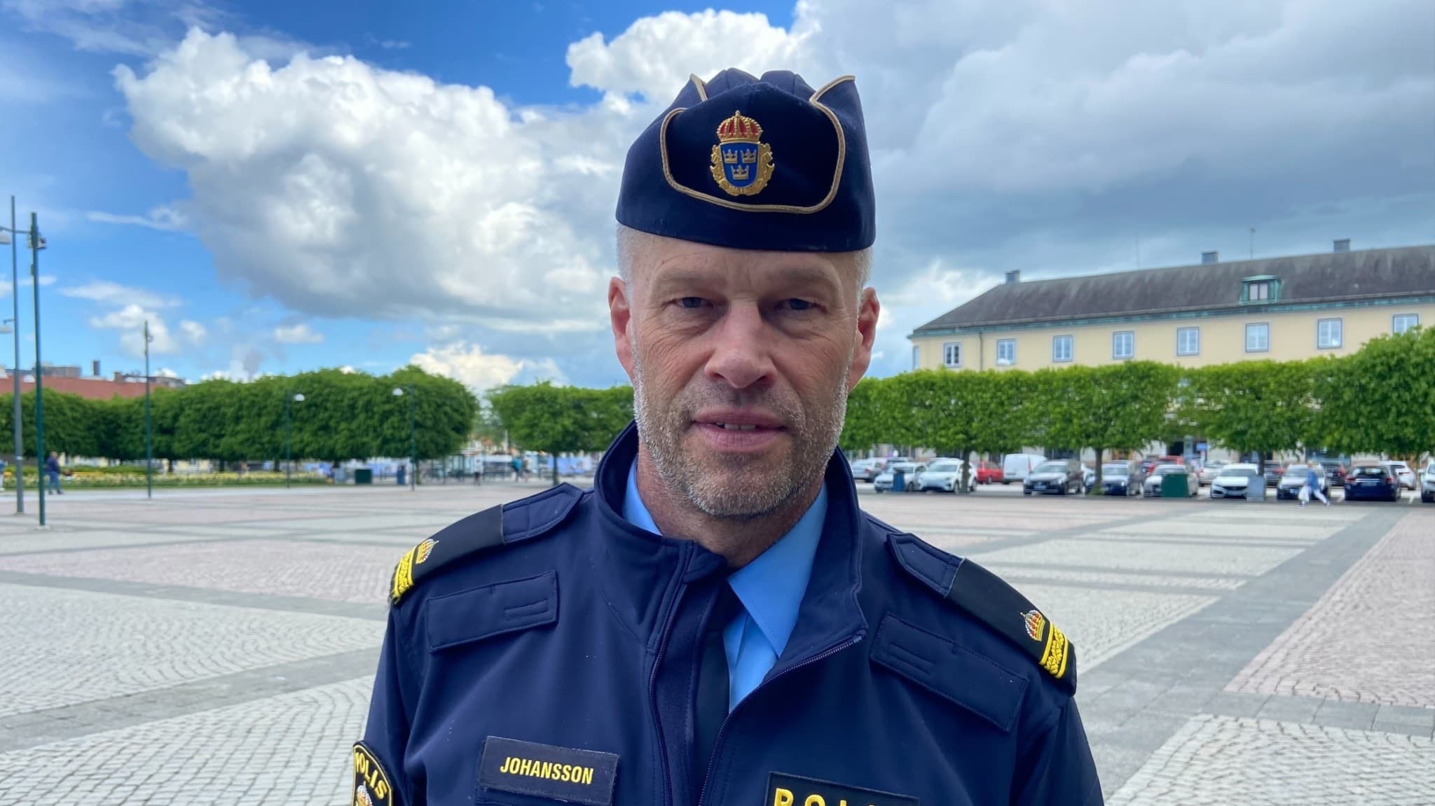 En polis står utomhus, i bakgrunden skymtar det bilar.