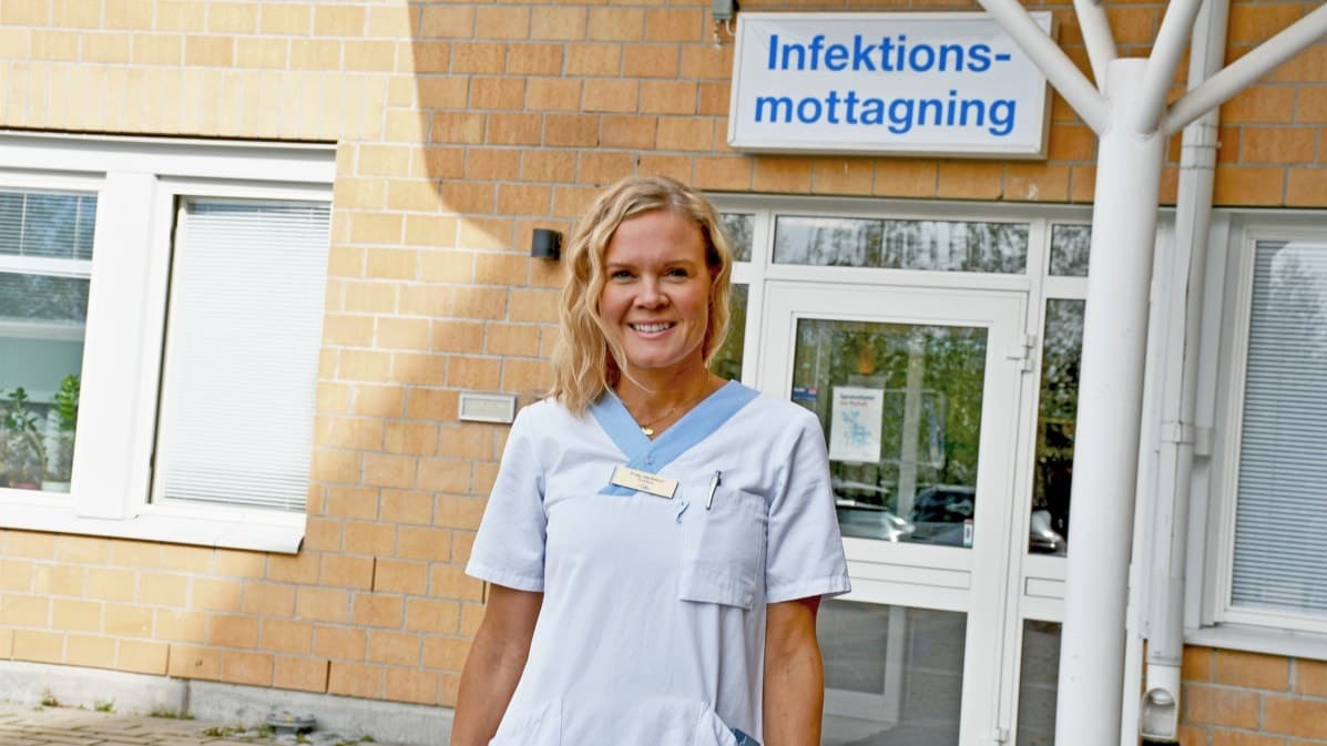 Smittskyddsläkare Frida Jakobsson står i vit läkarrock framför en byggnad med skylten 'Infektionsmottagning'.