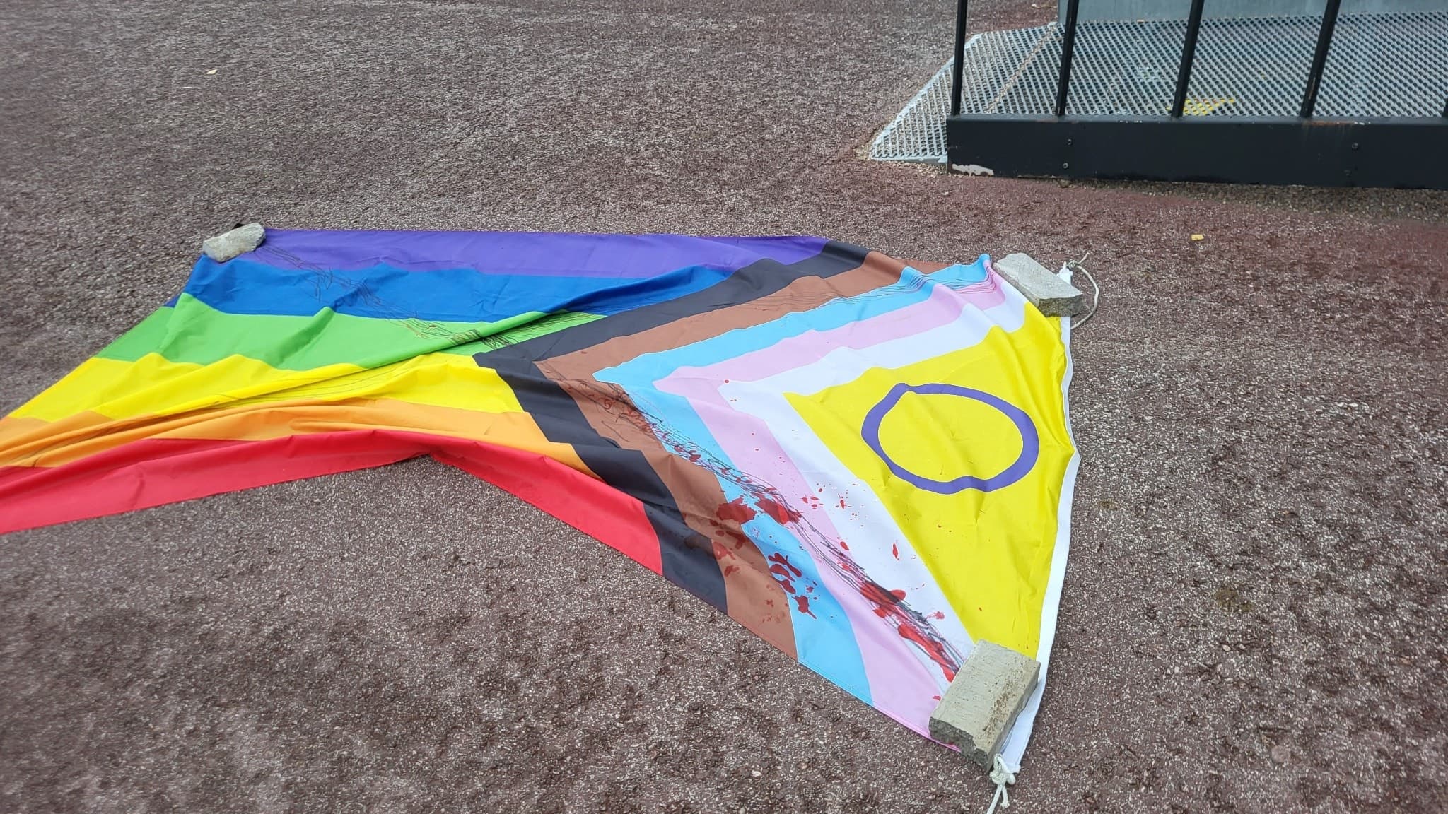 En Prideflagga med Progress-design ligger trasig på en grusplan i Överkalix. Flaggan visar tecken på vandalism och skador. 