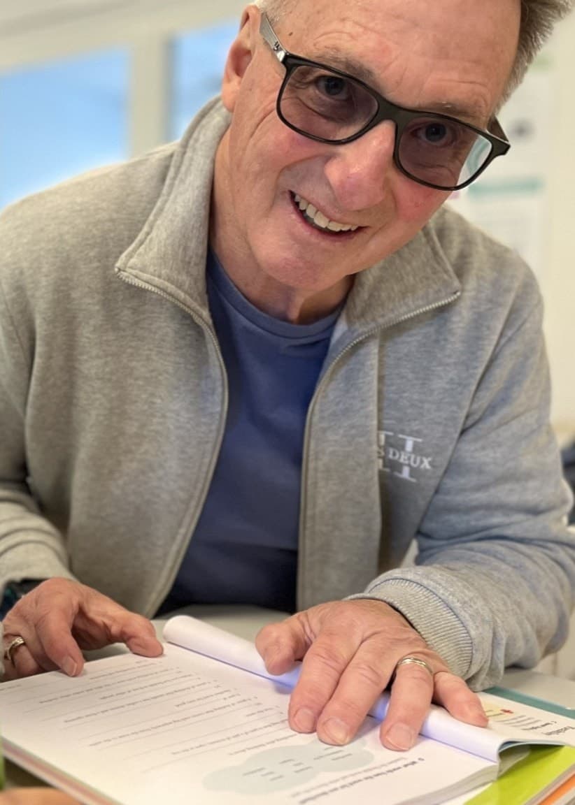 Peter, skolmorfar i Ekerö kommun, sitter vid ett bord och hjälper eleven Julian med skoluppgifter i ett klassrum.