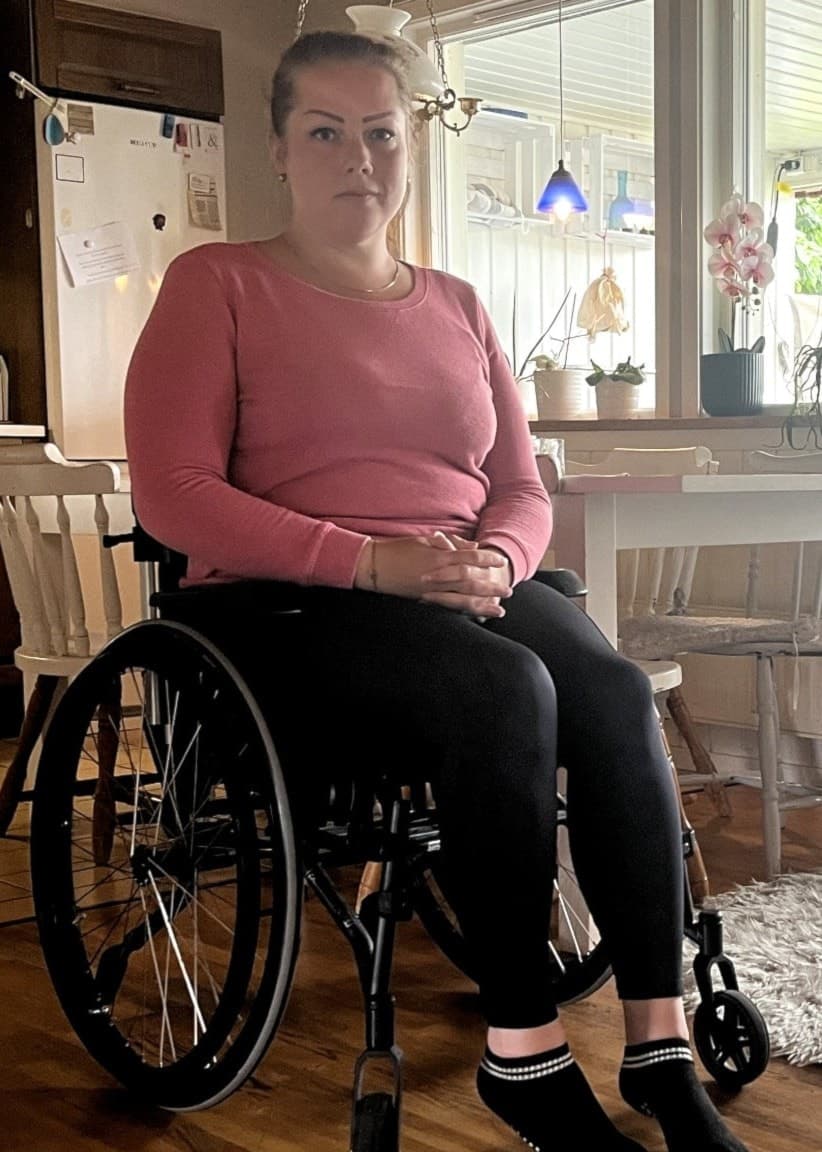 Angelica Henriksen sitter i rullstol i sitt kök efter en vårdskada. 