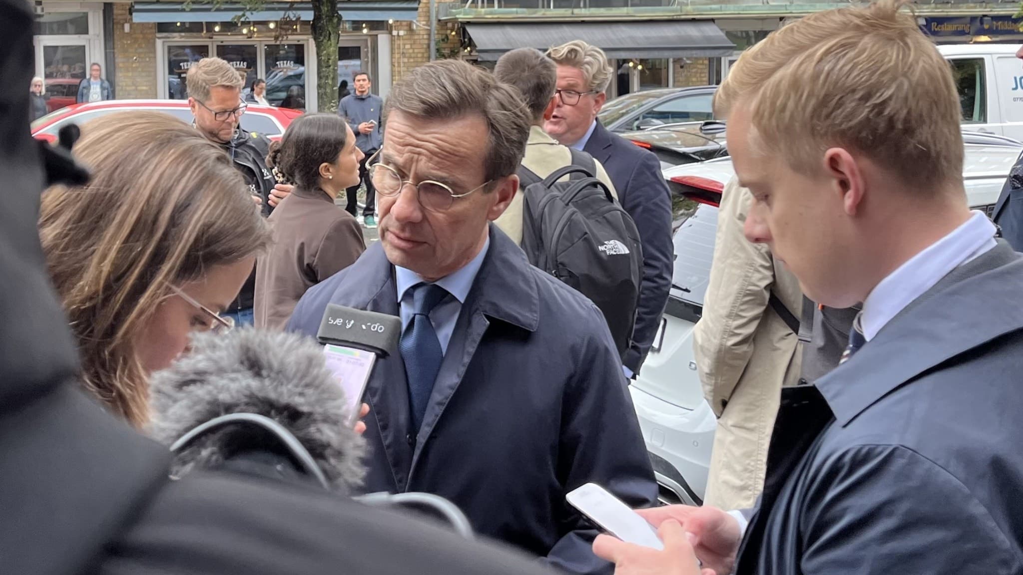 Statsminister Ulf Kristersson står vid flera journalister. Kristersson står utomhus med mikrofon mot sig.